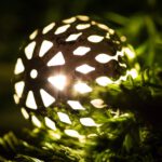 Eine von innen beleuchtete Weihnachtskugel liegt auf einem Tannenzweig.