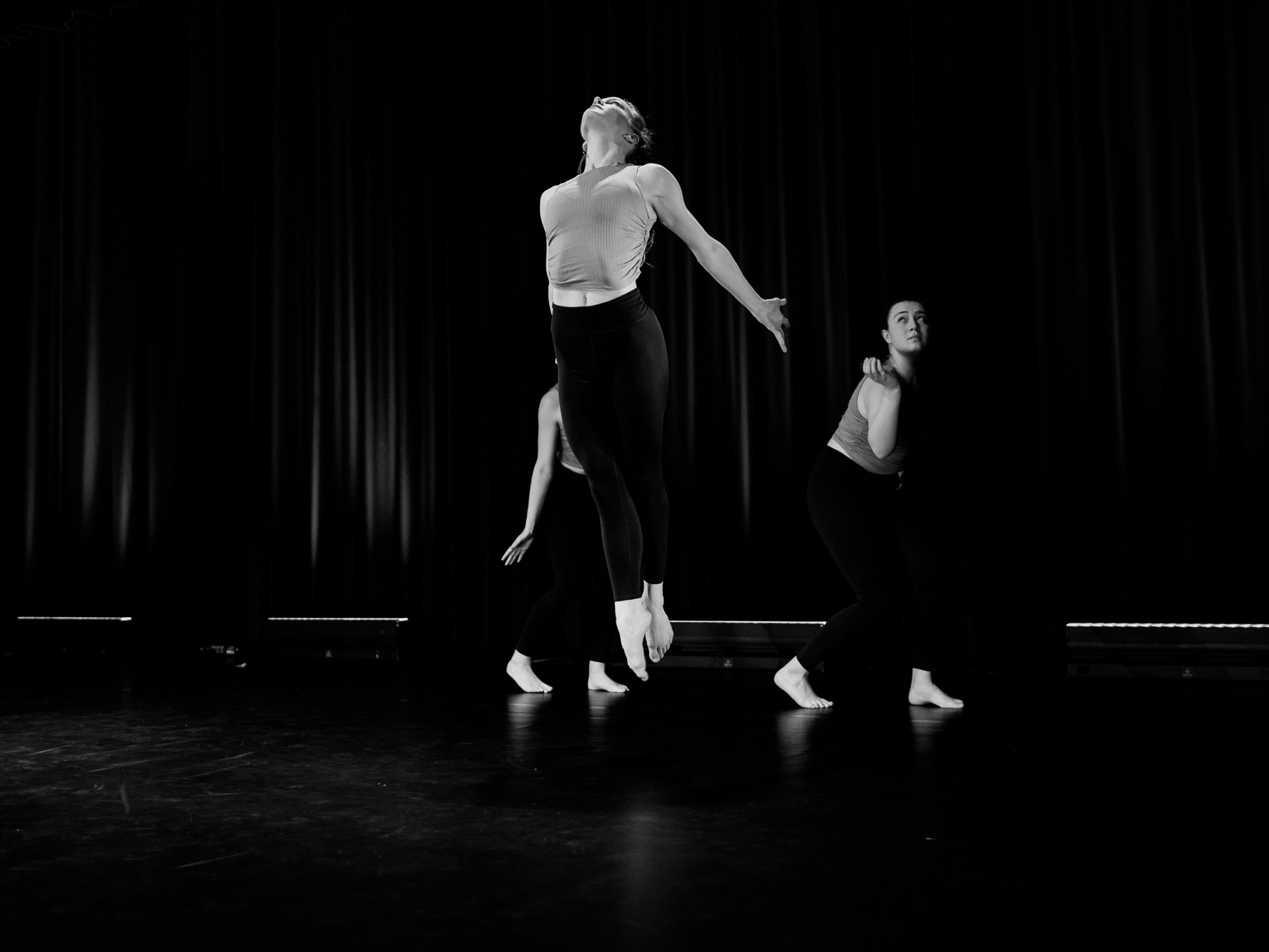 Schwarz-weiß Foto, das eine springende Tänzerin im Vordergrund und zwei gehende Tänzerinnen im Hintergrund zeigt.